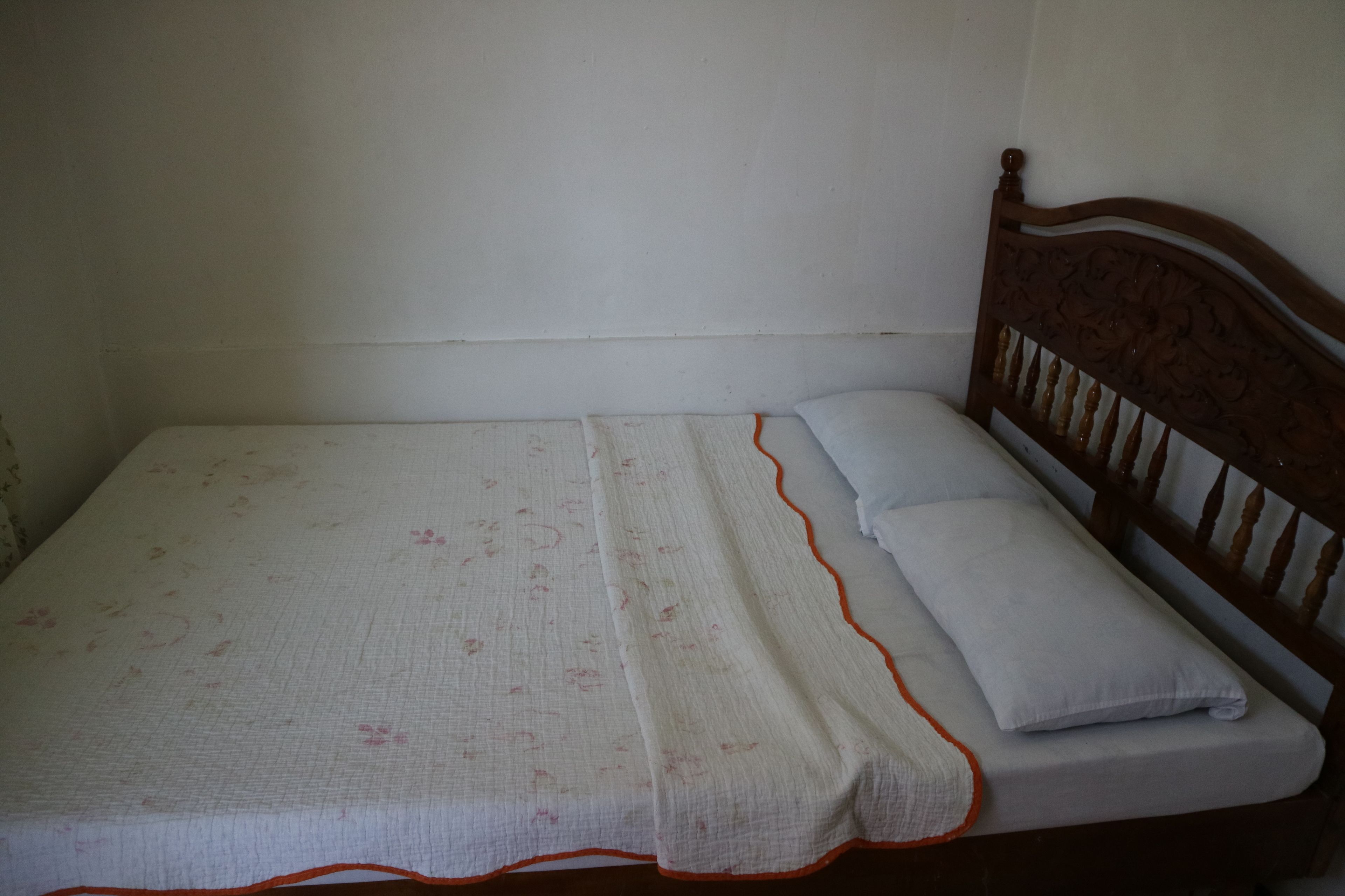 A single bed with a wooden headboard, a white bedspread with a floral pattern, and two pillows.