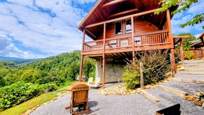 A wooden cabin with a balcony, surrounded by a gravel path and greenery.