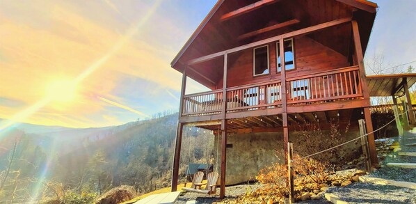 A wooden cabin with a balcony, surrounded by a mountainous landscape.