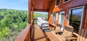 A wooden deck with outdoor seating and a hot tub, overlooking a forested landscape.