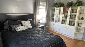 Une chambre à coucher avec un grand lit, une table de chevet, une bibliothèque et une fenêtre avec des rideaux.