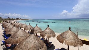 Une plage avec des parasols en chaume et des chaises longues.