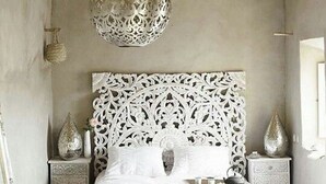Une chambre à coucher avec une tête de lit blanche ornée, une table de chevet assortie, une table de nuit et un miroir décoratif.