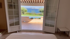 A bedroom with a large bed, a sliding glass door leading to a patio with a pool and a view of the sea. - Villa by the beach and with panoramic view on St Tropez (Grimaud)