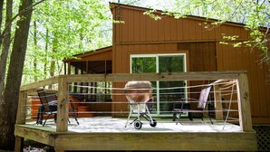 Een houten terras met een barbecue, stoelen en een tafel.