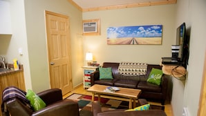 Een gezellige woonkamer met een bruine leren bank, een houten salontafel en een televisie op een dressoir.