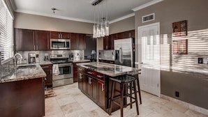 A modern kitchen with dark wood cabinets, stainless steel appliances, a marble countertop, and a central island with bar stools. - Resort Style 3 Bed, 3 Baths, Private Pool - Family Friendly -  Special CAD rate (Glendale)