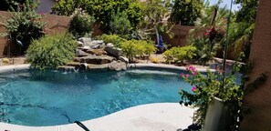 Une piscine agrémentée d’un élément rocheux, entourée de différentes plantes et d’une petite cascade.