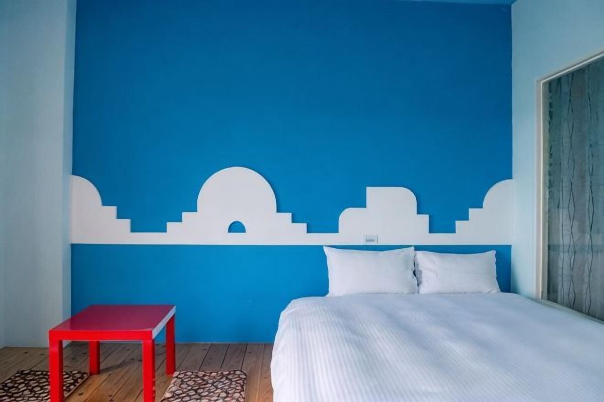 A bedroom with a bed, a red table, and a blue wall with white architectural designs.