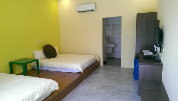 Un dormitorio con cama, una mesita de noche verde, un baño con lavamanos y espejo, y un escritorio pequeño con silla.