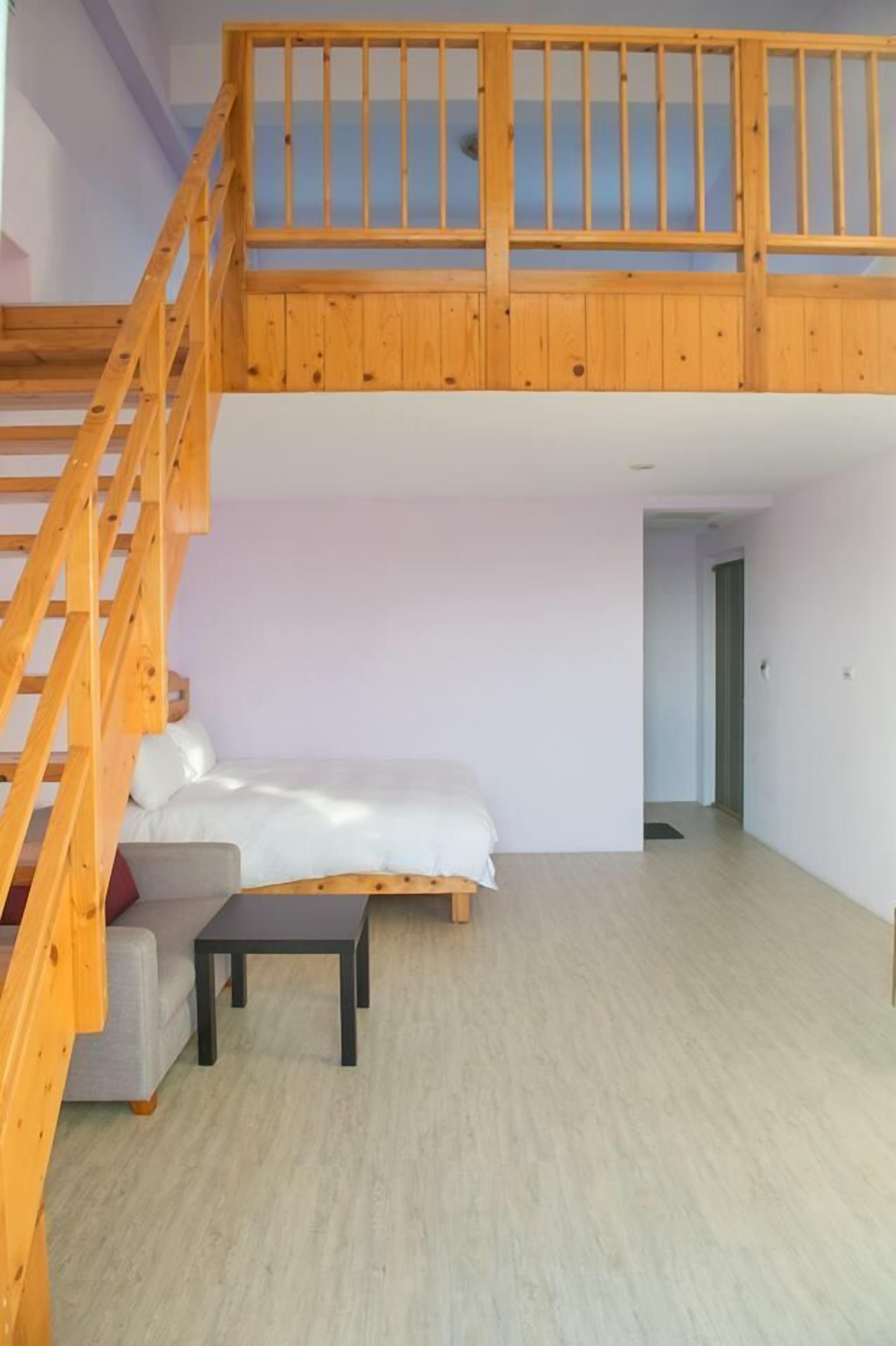 A spacious room with a loft bed, a wooden staircase, a small table, and a sofa.