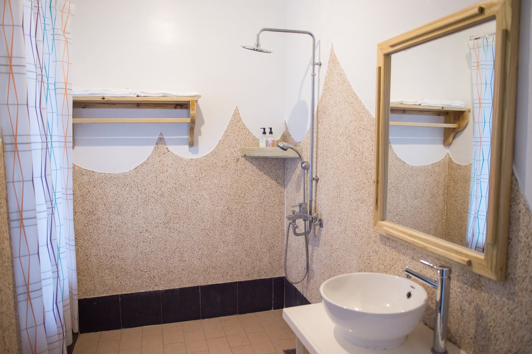 Ein Badezimmer mit weißem Waschbecken, einer Dusche mit Duschbrause und einem Spiegel mit Holzrahmen.