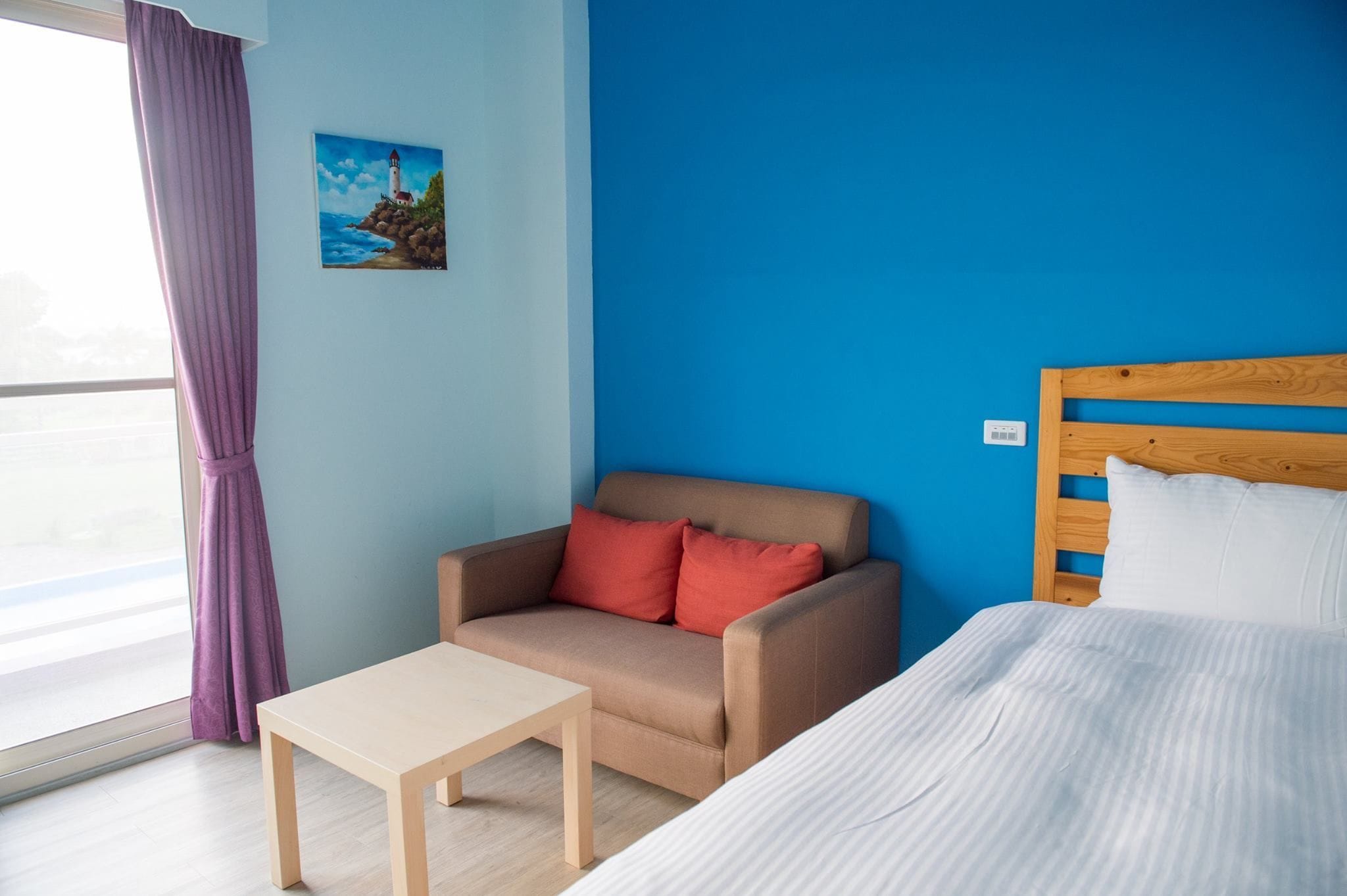 A room with a bed, a sofa, a small table, and a painting on the wall.