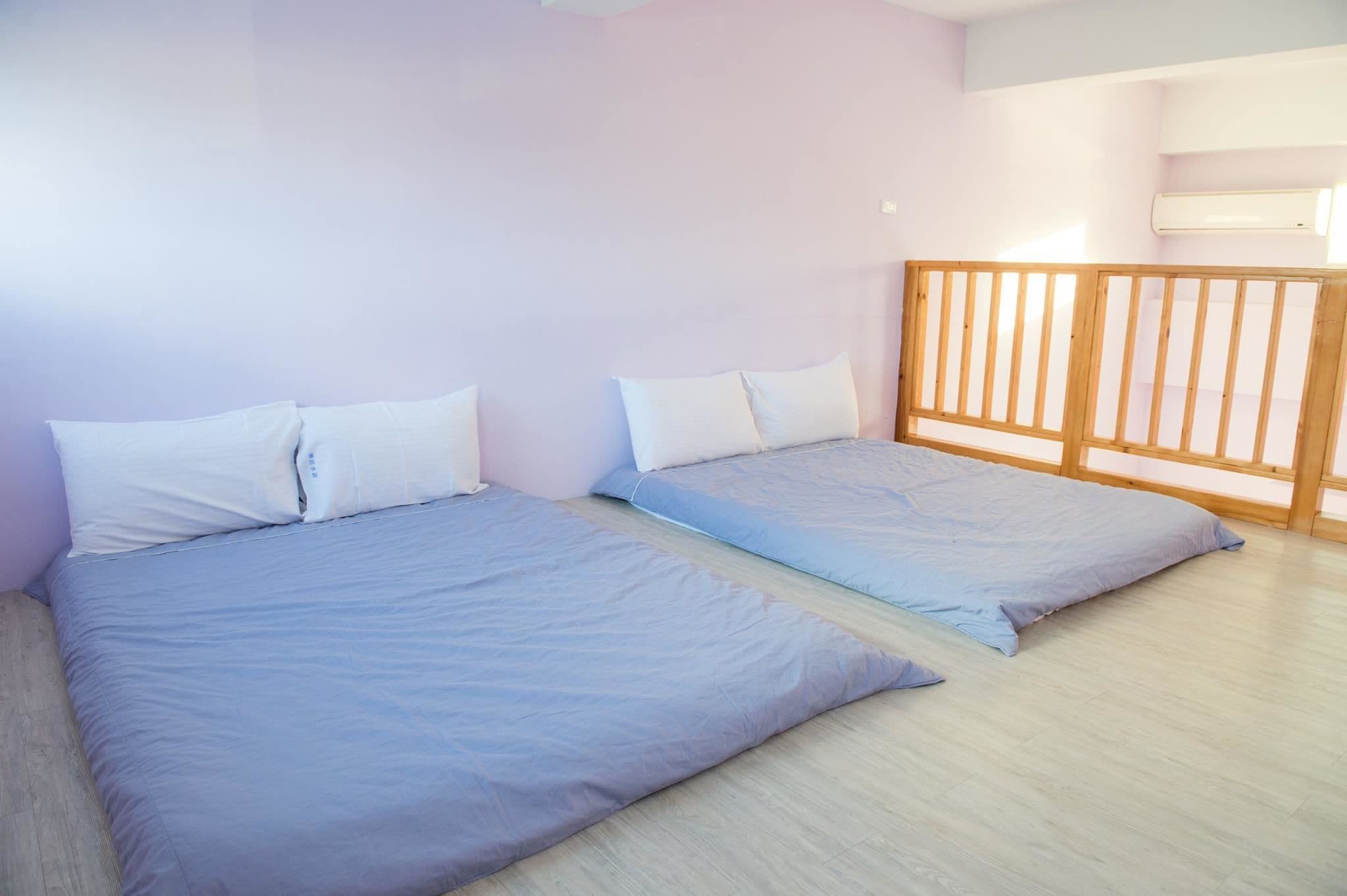 A room with two beds, light-colored walls, and a wooden railing.