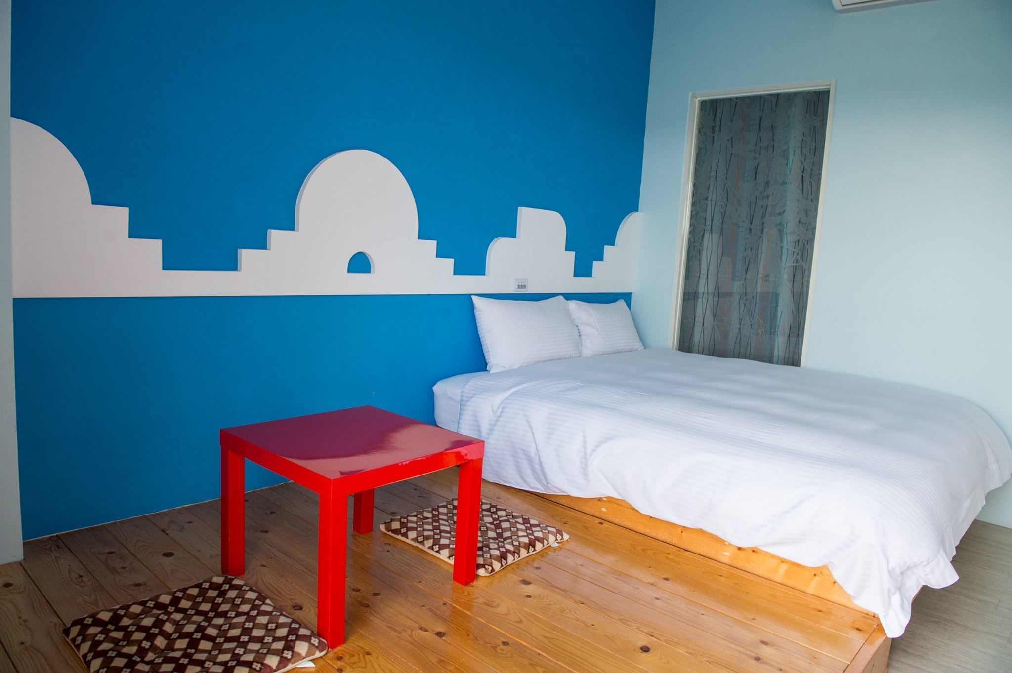 A bedroom with a bed, a red table, and a blue wall with white cut-out cityscape design.