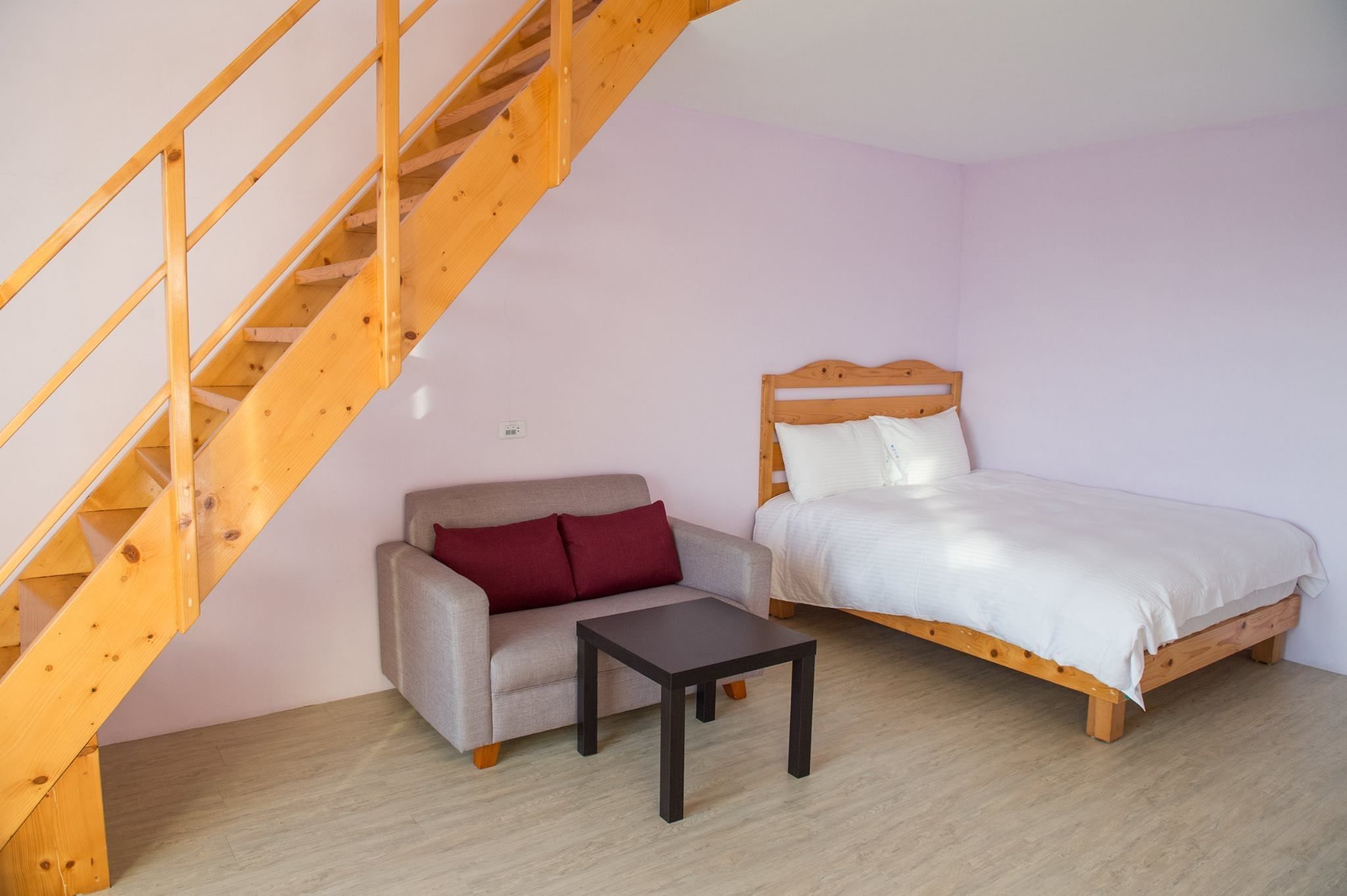 Habitació amb escala de fusta, llit, sofà i taula petita.