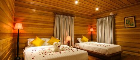 A wooden cabin-style room with two beds, each with white bedding and yellow pillows. There are two bedside lamps, a ceiling light, and a framed picture on the wall.
