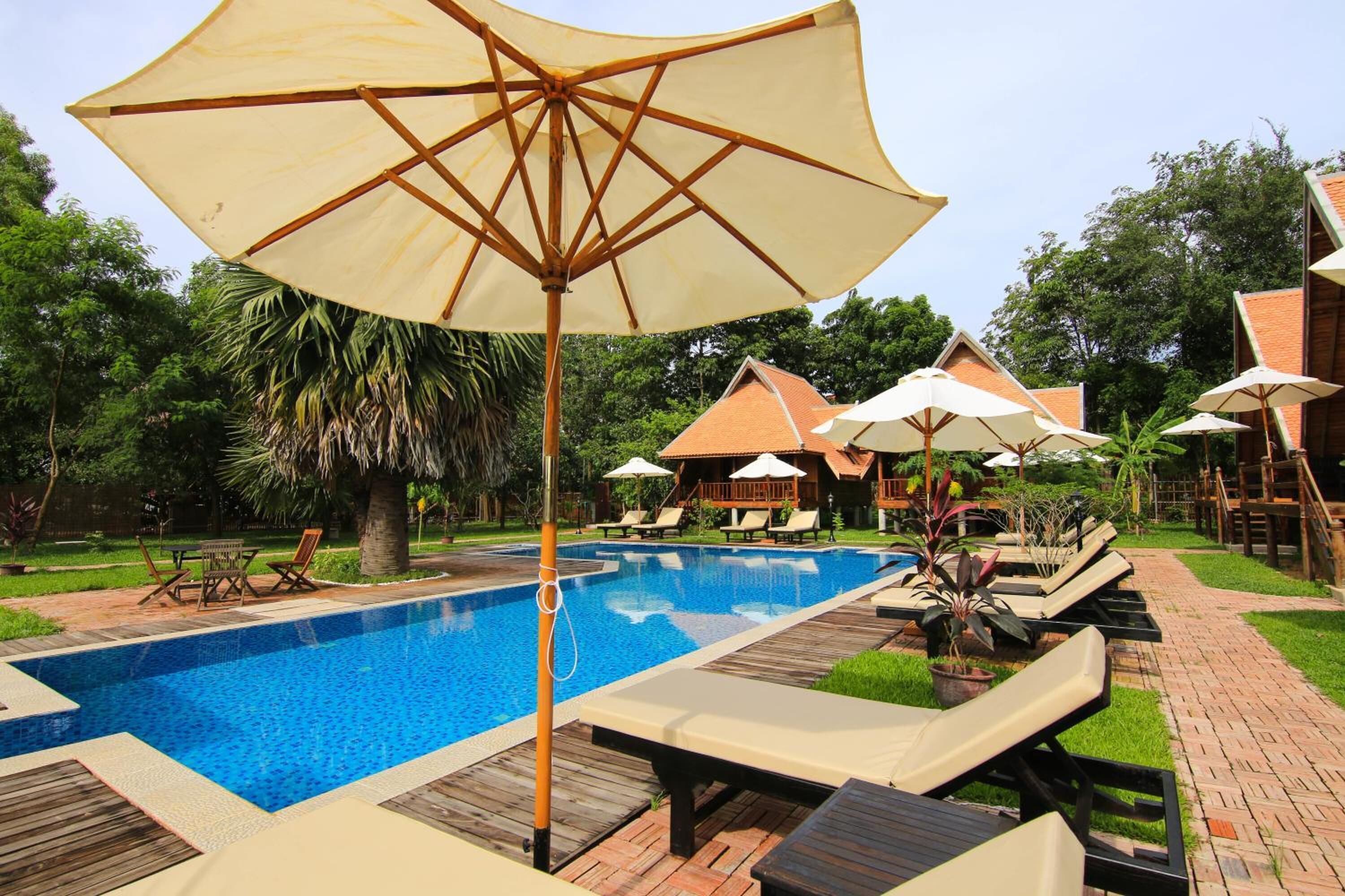 A swimming pool with lounge chairs and umbrellas, surrounded by greenery and a brick pathway.