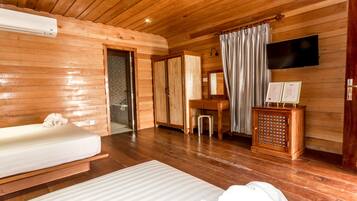 Een houten kamer met een bed, een bureau, een televisie en een klein kastje.