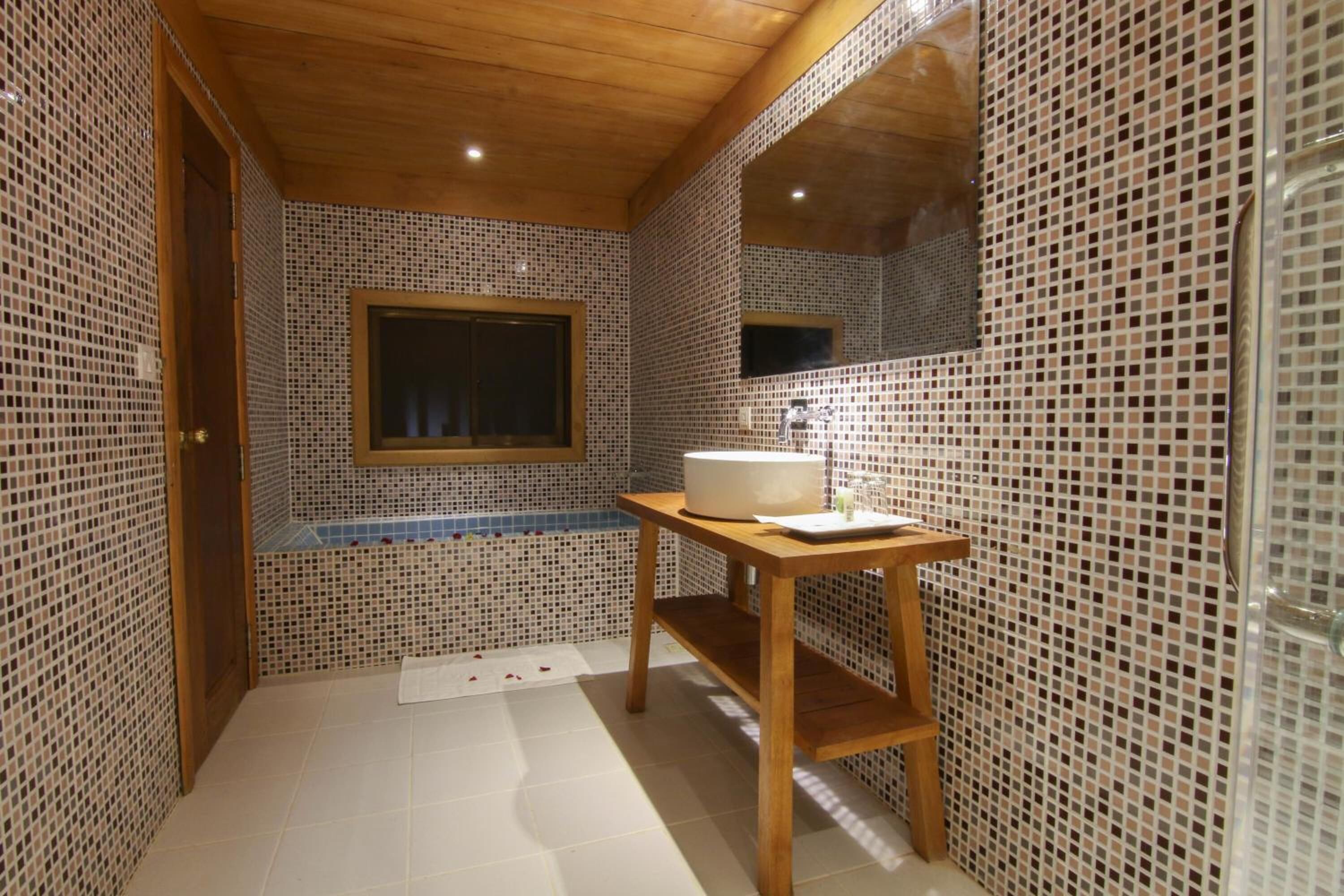 A bathroom with mosaic tile walls, a wooden bench, a sink, and a window.