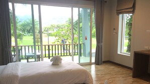 A hotel room with a large bed, a small table, and a view of a garden through a sliding door. - Khaolak Mountain View (Takua Pa)