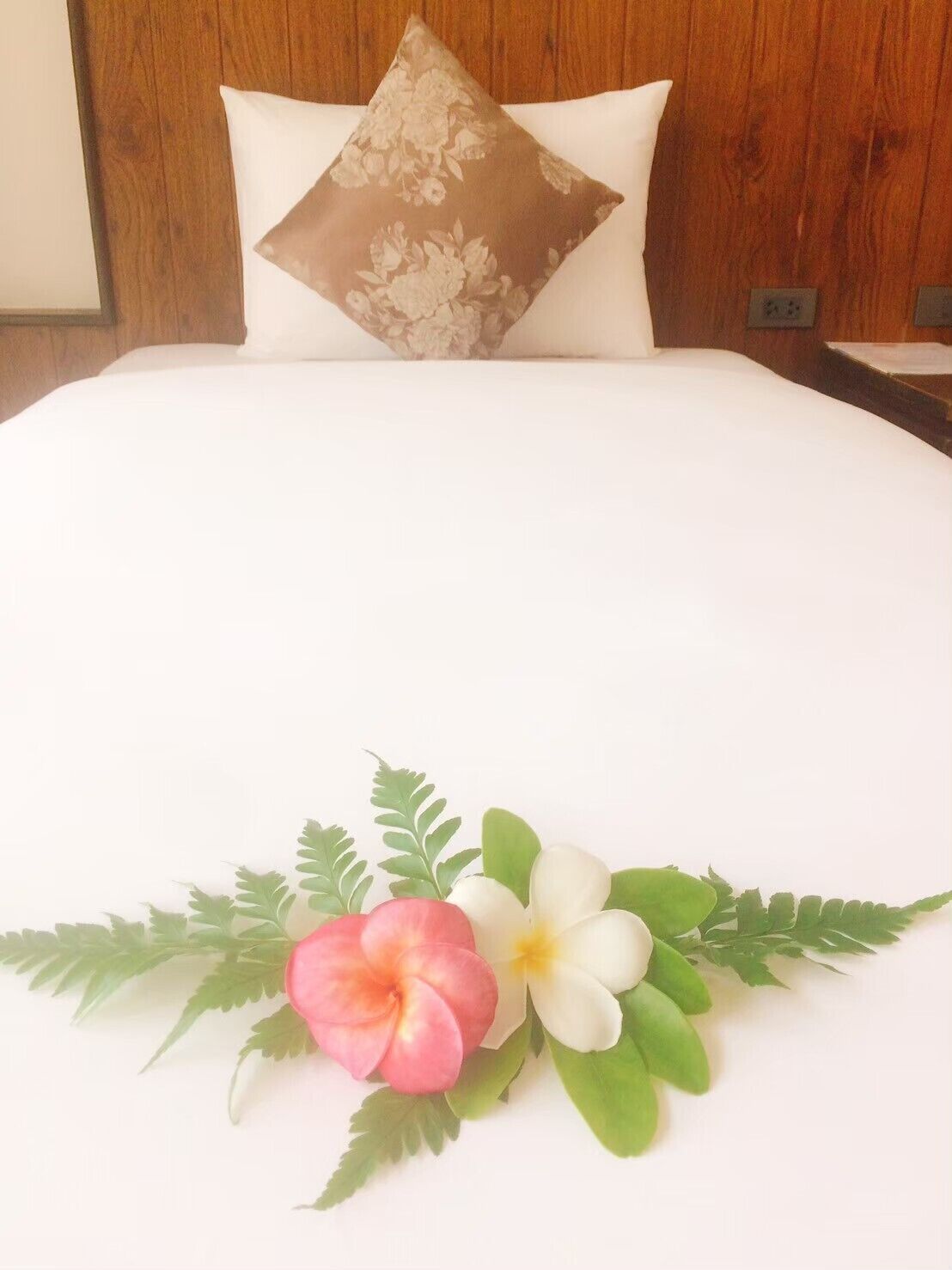 Una cama bien hecha con un cojín floral y un arreglo decorativo de flores y hojas sobre la colcha.
