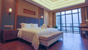 Moderni hotellihuone, jossa on suuri sänky, yöpöytä, penkki ja suuret ikkunat, joista avautuu näkymä kaupunkiin.