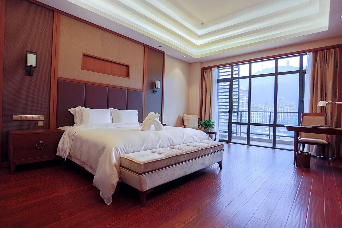 Ein geräumiges Hotelzimmer mit einem großen Bett, einem Schreibtisch und Blick auf die Stadt durch große Fenster.