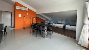 A spacious room with a long table and chairs, a bed with a blue headboard, and an orange accent wall. - Mangyi Inn (Hengchun)