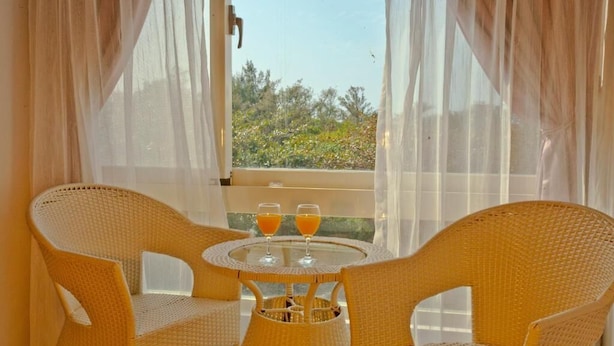 A balcony with wicker chairs and a table, two glasses of orange juice, and a view of greenery. - Mangyi Inn (Hengchun)