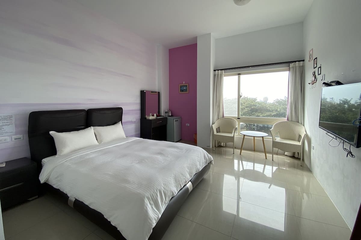 Habitación de hotel moderna con una cama grande, un escritorio, una silla, un televisor y un balcón con vistas.