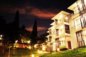 A modern multi-story building with balconies and large windows, surrounded by a well-lit garden area. - Lembang Asri Resort (Parongpong)