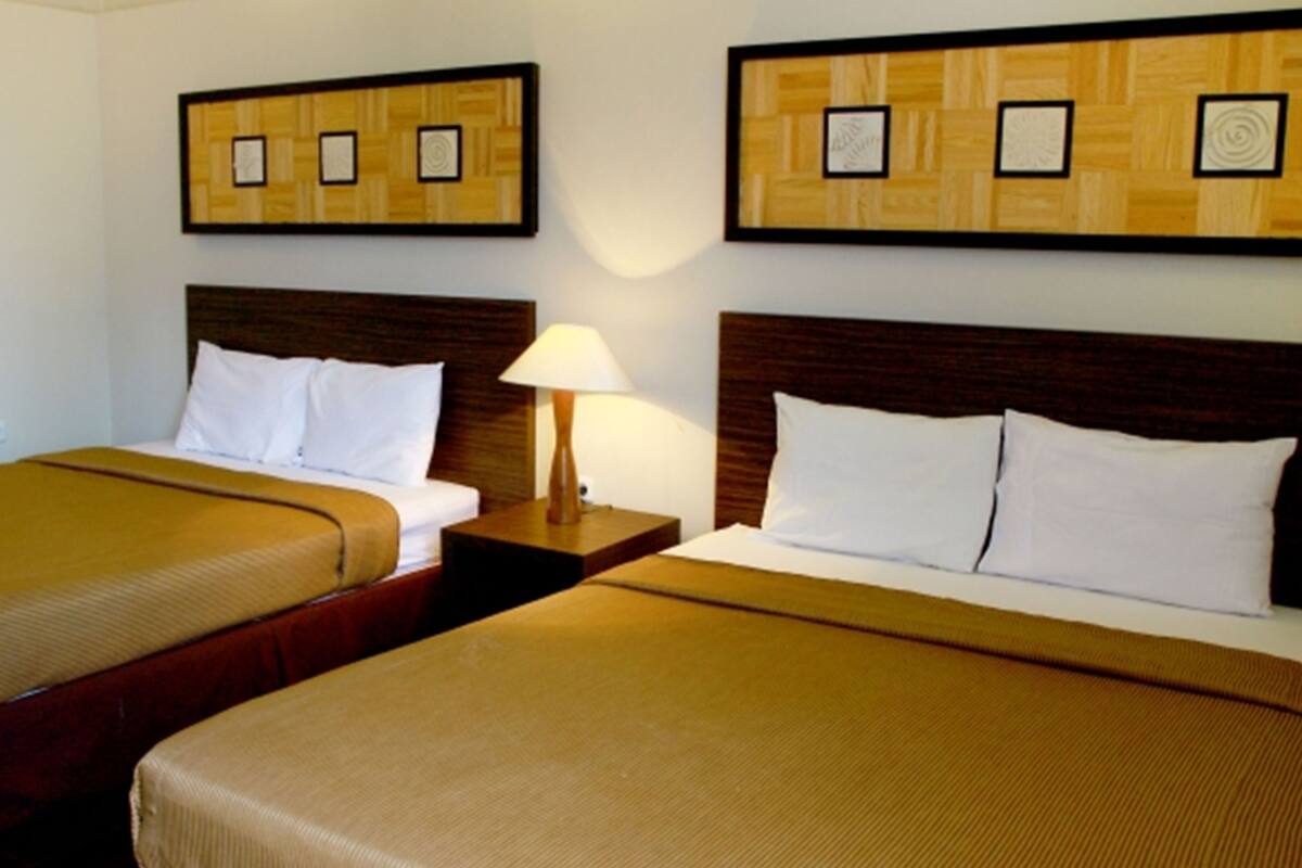 Ein Hotelzimmer mit zwei Betten, einem Nachttisch mit Lampe und einer Wand mit gerahmten Kunstwerken.
