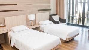 Habitación de hotel con dos camas, una mesita de noche con lámpara, una silla de mimbre y un gran ventanal con vistas.