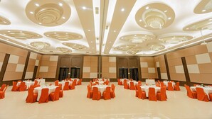 Una espaciosa sala de conferencias con varias mesas redondas, cada una rodeada de sillas naranja, y un diseño de techo moderno con luminarias circulares.
