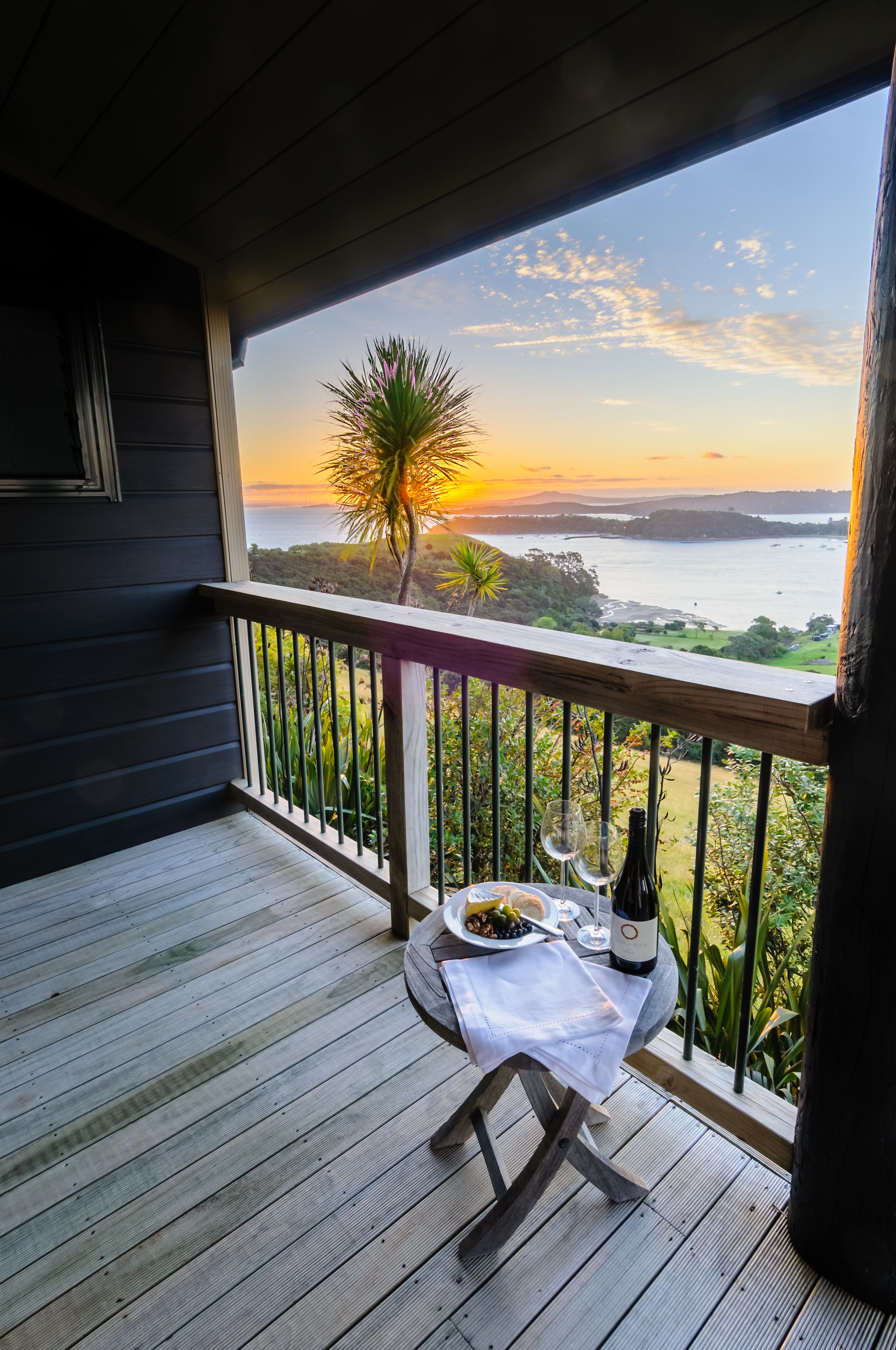 A balcony with a table set for two, overlooking a scenic view of the sunset over water.