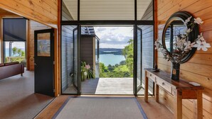 A modern interior with a large glass door leading to a balcony with a lake view. - Te Whau Lodge (Waiheke Island)