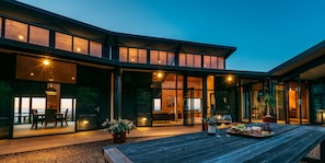 A modern house with large glass windows, a wooden deck, and a dining area with a table set for two. - Te Whau Lodge (Waiheke Island)