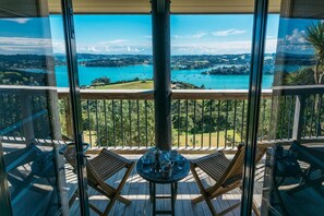 Un balcón con una mesa dispuesta para dos personas, con vista a un paisaje pintoresco de un lago y sus alrededores.