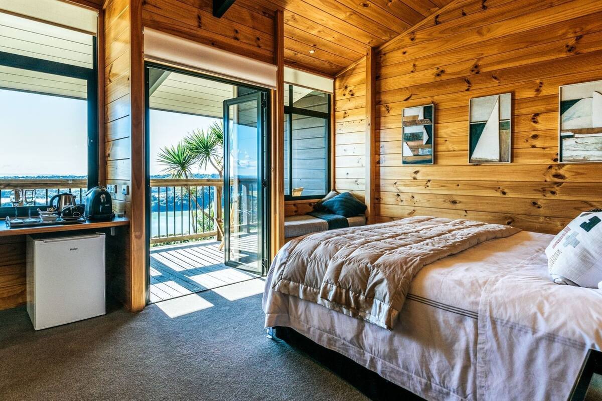 A wooden cabin bedroom with a bed, a desk, and a small kitchenette.