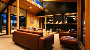 A modern living room with leather sofas, a fireplace, and a bookshelf. - Te Whau Lodge (Waiheke Island)