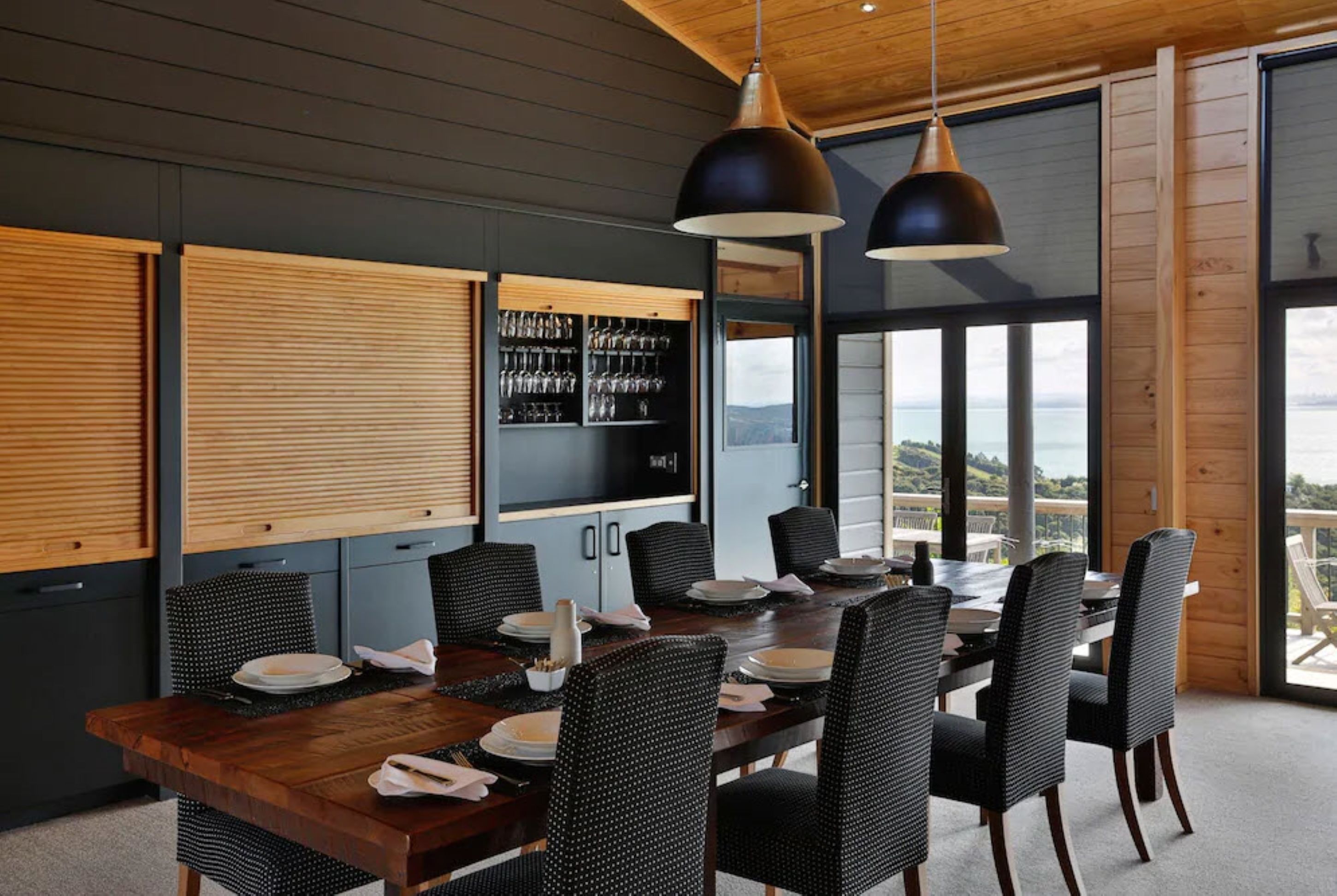 Uma sala de jantar com mesa de madeira, cadeiras de vime preto e iluminação pendente.