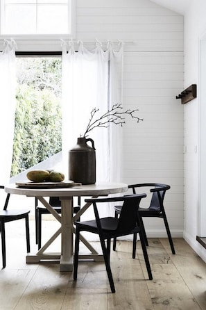 A dining area with a round table, black chairs, a vase with branches, and a window with curtains. - The Bower Byron Bay (Byron Bay)