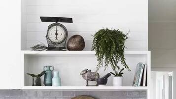 A kitchen with white cabinetry, a marble countertop, a scale, a plant, decorative items, and a brick backsplash.