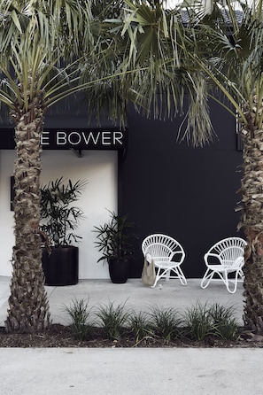 A storefront with a black facade and the name "BOWER" in white letters. There are two white wicker chairs in front of the store, and a palm tree to the left. - The Bower Byron Bay (Byron Bay)