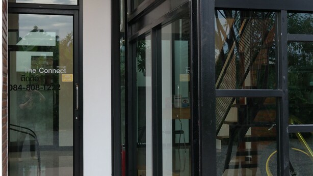 A modern building entrance with glass doors and windows, a visible staircase, and a contact number on the door. - The Connect Chiang Mai (Chiang Mai)