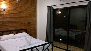 A hotel room with a brick wall, a bed with white linens, a sliding glass door leading to a balcony, and an air conditioning unit on the wall. - The Connect Chiang Mai (Chiang Mai)