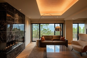 Una sala de estar moderna con chimenea, un sofá, una mesa de centro y ventanas amplias que ofrecen vistas al exterior.