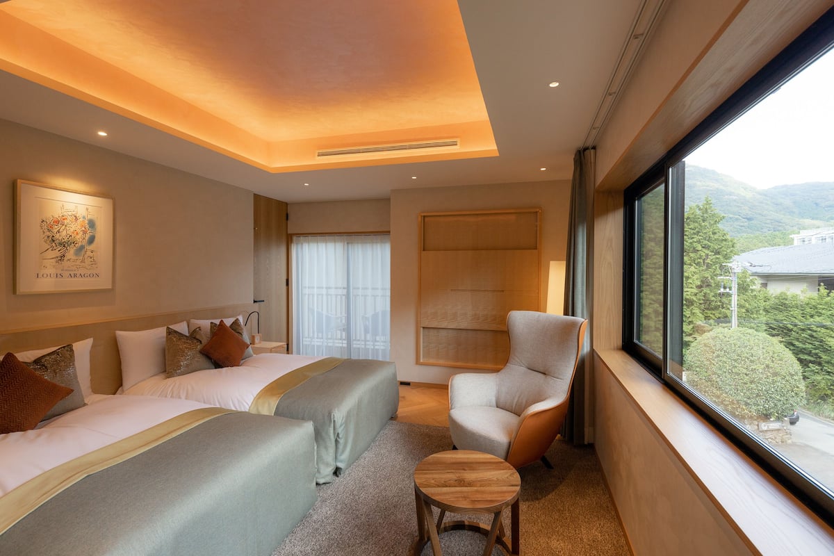 Ein modernes Hotelzimmer mit zwei Betten, einer Sitzecke und einem großen Fenster mit Blick ins Freie.