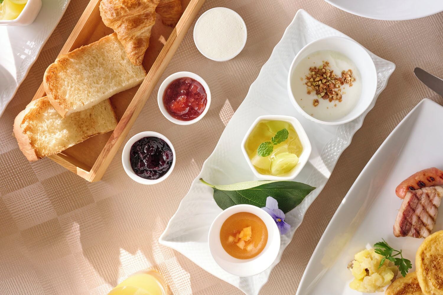 Un desayuno con cruasanes, mermeladas, yogur y una variedad de frutas y verduras.